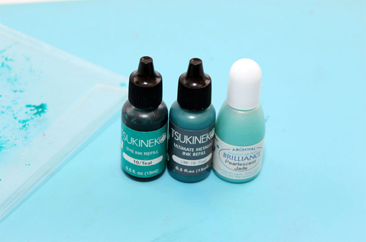 Tsukineko dye inker, metallic inker and brillicance inkers in teal colors lined up in a row.