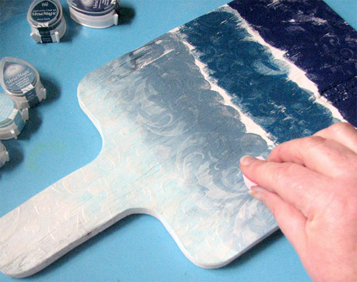 Roni Johnson applies and blend VersaMagic inks to a wood cutting board she is repurposing.